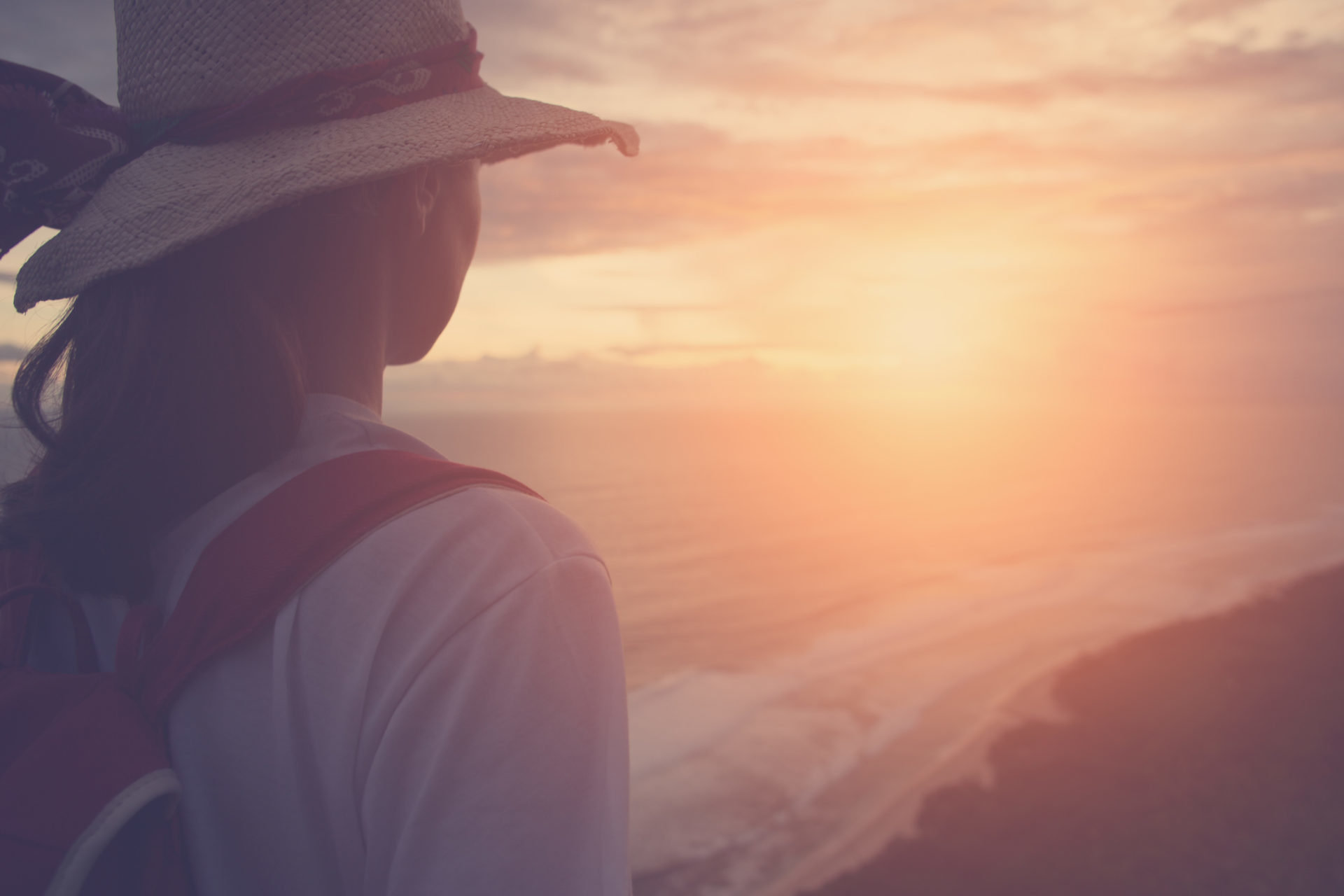 Silhouette of girl wearing hat looking far away at sunset on a beach from a high (intentional sun glare and vintage color)